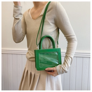 Detailed view of a green handbag with a clear PVC window and smooth leather finish