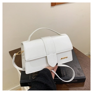 Détail du petit sac blanc en cuir avec logo JINGPIN doré posé sur des livres reliés