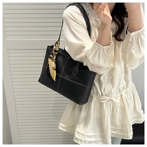 Detail of black leather tote bag with white contrast stitching and silk scarf handle decor