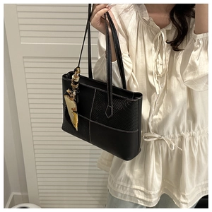 Detail of a black patchwork tote bag with snakeskin texture and yellow silk scarf