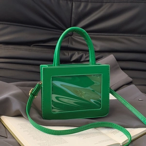 Minimalist bright green crossbody bag with clear window and round handle on black leather sofa