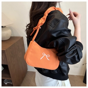 Close-up of orange hobo bag with white bow print worn by model in a minimalist setting