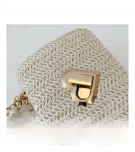 Detailed close-up of straw woven bag with heart-shaped gold clasp and pearl chain strap