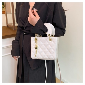 Detailed shot of white quilted patent leather bag with gold key pendant and handle