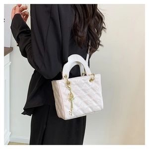 Close-up of white quilted patent leather handbag with dual handles and gold key charm