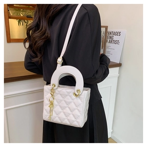 Detailed view of a white quilted crossbody bag with gold charm and round handles