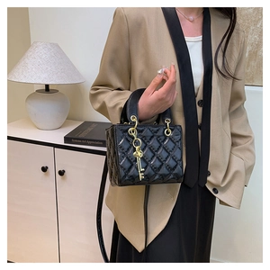 Detail of black quilted leather handbag with gold key charm and crossbody strap