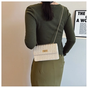 Detail of cream straw woven square bag with gold chain strap and twist lock on a model