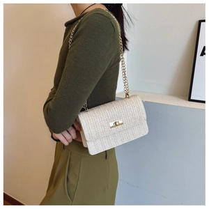 Detail of woven texture and golden chain on beige straw shoulder bag worn by model