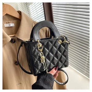 Close-up of black patent leather crossbody bag with quilted pattern and gold buckle hardware