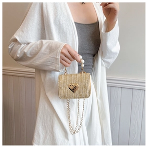 Detail of beige straw crossbody bag with pearl handle and golden heart lock