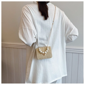 Detail of a beige woven mini bag with pearl handle and golden chain strap on model