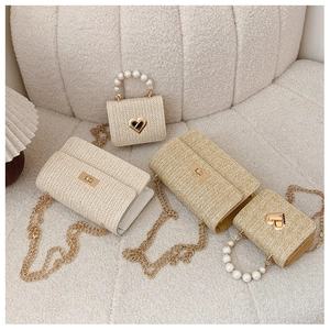 Macro detail of woven straw bags with golden chain and pearl handle on beige sofa
