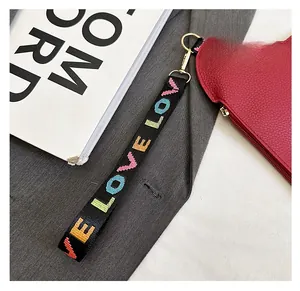 Close-up of a red lychee texture leather pouch with a colorful LOVE woven wristlet strap