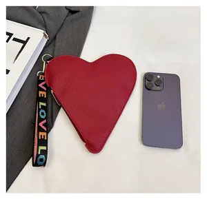 Red heart-shaped leather clutch bag with colorful LOVE strap next to a phone for scale