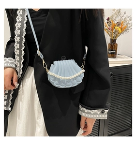 Detail view of light blue shell-shaped handbag with decorative pearl chain and slim strap