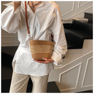 Detail of straw bucket bag with beige stripes, leather strap and silver hardware accents