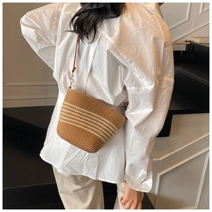 Detail of woven straw crossbody bag with brown leather strap worn by a model