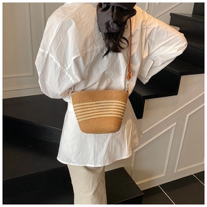 Detail of hand-woven straw bucket bag in dark brown with cream stripes and leather strap