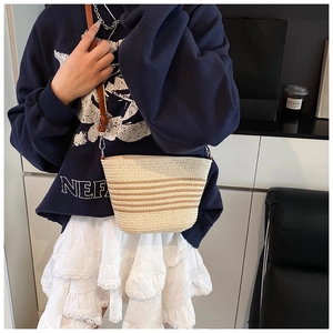 Detail of hand-woven straw bucket bag with brown stripes and leather shoulder strap