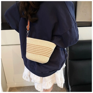 Detail of a beige woven straw bucket bag with brown horizontal stripes and leather strap