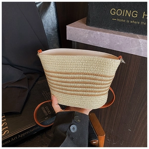 Detail of hand-woven striped straw bucket bag featuring contrast brown shoulder strap
