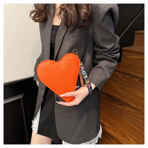 Detail of a bright orange heart-shaped clutch bag in lychee pattern with a LOVE wrist strap
