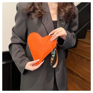 Detail of orange heart-shaped clutch with lychee pattern and LOVE printed wrist strap