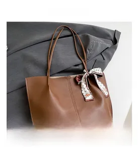 Detail of brown faux leather tote bag featuring vertical stitching and a floral silk scarf