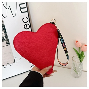 Détail de la pochette rouge en forme de cœur avec texture litchi et dragonne LOVE brodée