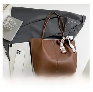 Detail of a brown leather tote bag with a geometric silk scarf on the handle and a smooth finish