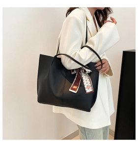 Detail of black leather tote bag with stylish patterned silk scarf on a white blazer