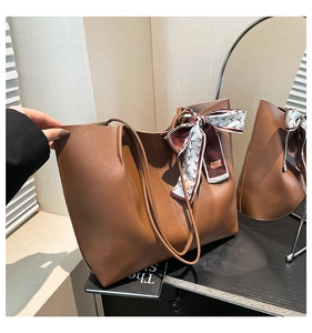 Detail of a brown tote bag featuring textured leather and a stylish silk scarf bow accent