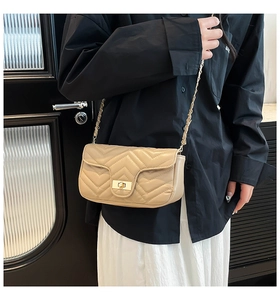 Close-up of beige quilted crossbody bag with gold turn-lock and chain strap on a model