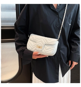 Detail of white quilted handbag with gold clasp and leather-woven metal chain