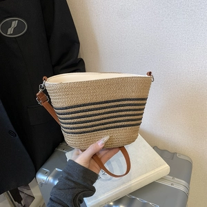 Beige striped straw bucket bag with brown leather handles and casual vacation style