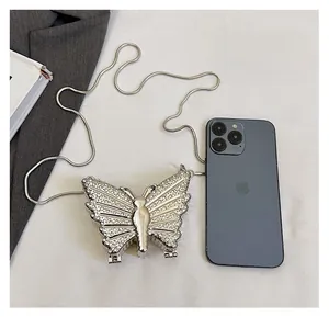 Detail view of silver butterfly chain bag with rhinestones next to a phone for size comparison