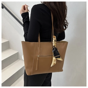 Brown leather tote bag with silk scarf detail worn by model on a white background