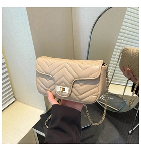 Detail der beigen Stepptasche mit V-Naht, goldenem Drehverschluss und goldener Kette