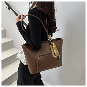 Detail of a brown tote bag with white stitching and decorative silk scarf accessory
