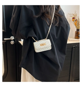 Detail of cream quilted mini crossbody bag with gold chain strap on model shoulder