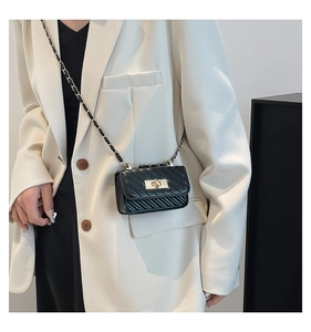 Close-up of black quilted mini bag with gold chain strap worn by a model in a white blazer