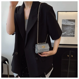 Detail of silver sequin mini bag with gold chain and metal lock worn on black blazer