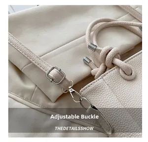 Detail view of the silver adjustable buckle and lobster clasp on a beige leather bag