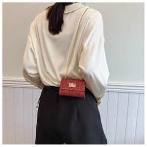 Detail of red glitter mini crossbody bag with gold chain strap on model's shoulder