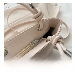 Close-up of beige lychee texture handbag featuring smooth metal zipper and knot handle