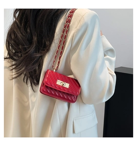 Detail of red quilted mini crossbody bag with gold chain strap worn by a model in white