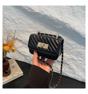 Detail of black quilted mini bag with gold twist lock and woven chain strap held in hand