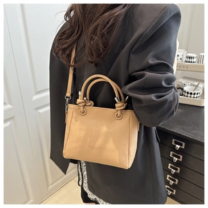 Détail du sac seau en cuir marron clair porté en bandoulière avec logo texte tendance