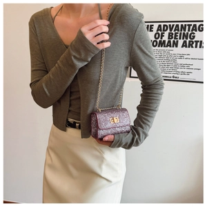 Close-up of sparkling purple mini bag with gold chain strap on a green sweater